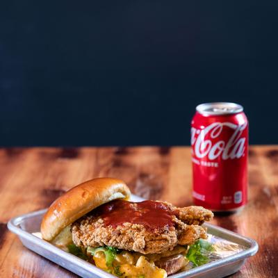 Mac Fried Chicken sandwich on a plate, accompanied by a soda can