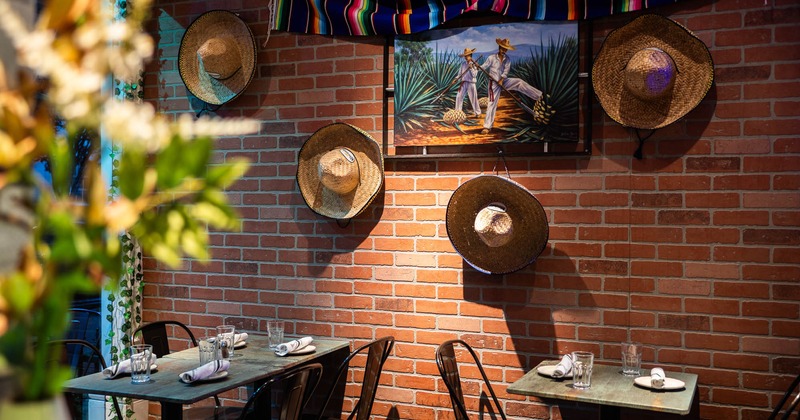 Interior, red brick wall, tables for two, straw hats and painting hanged as a decoration