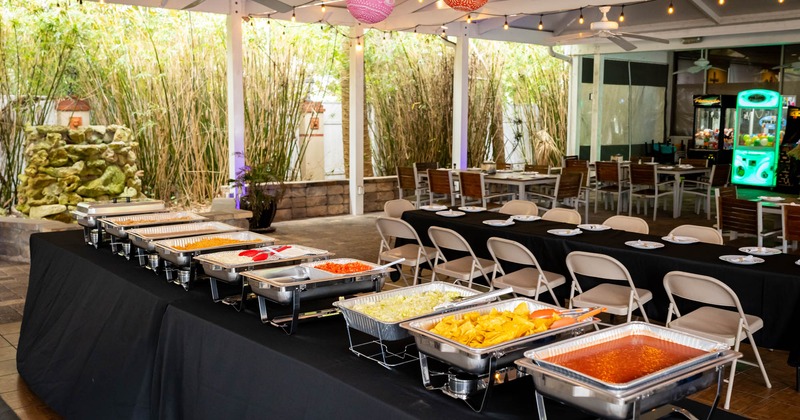 Exterior, patio, catering trays filled with food, seating area, lanterns on the ceiling