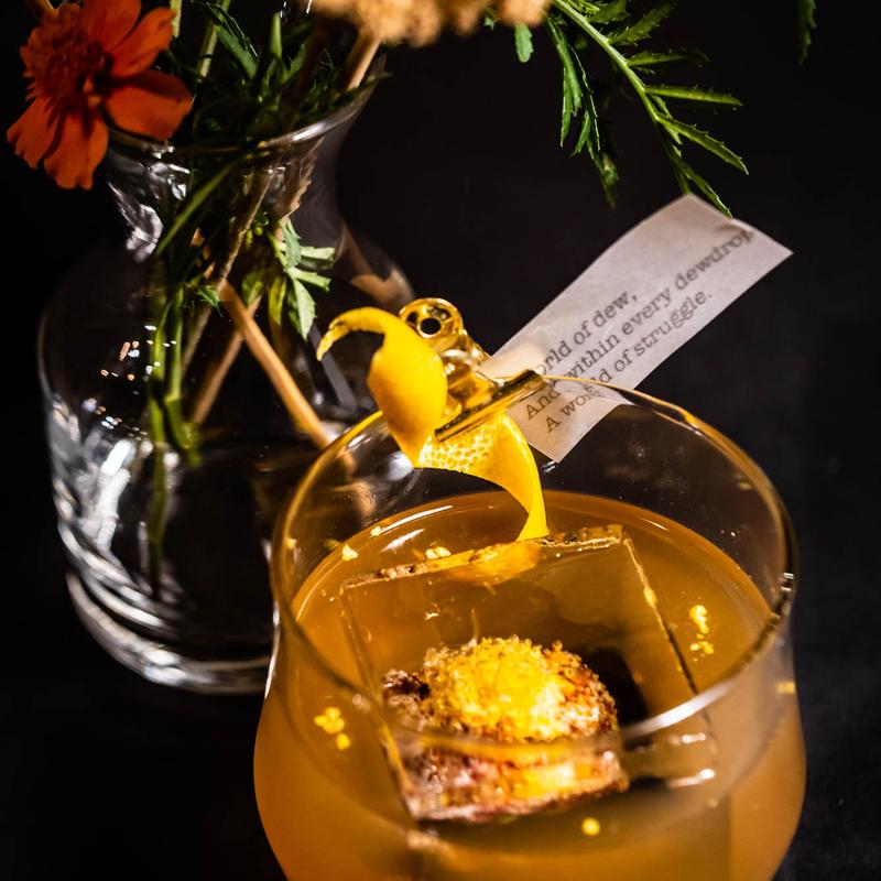 An orange cocktail with orange peel garnish.