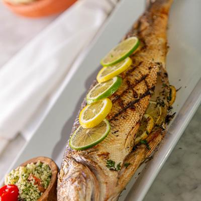 Grilled whole fish, topped lemon and lime wedges, served with a rice salad