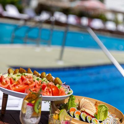 Outside, sushi and fruits on a table by a swimming pool