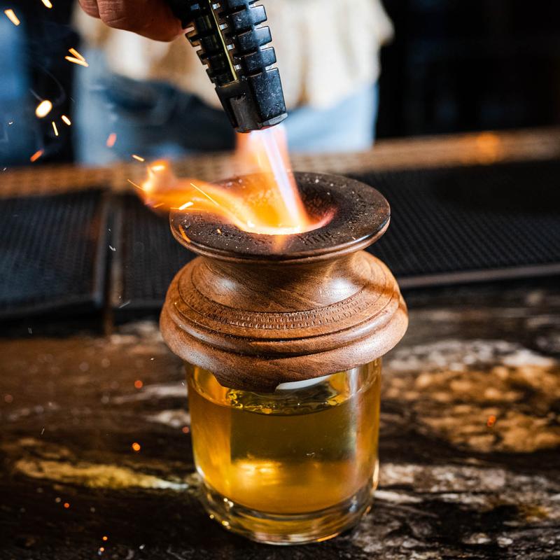 Bartender burning the smoke top on a cocktail drink, closeup