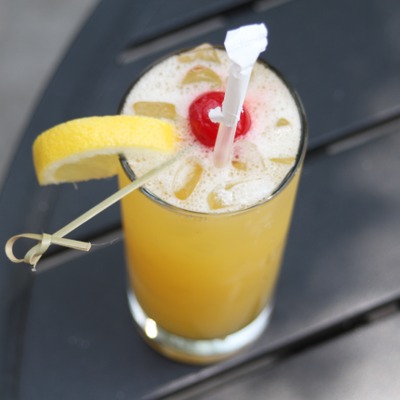 Foamy yellow cocktail with decorations and a cherry