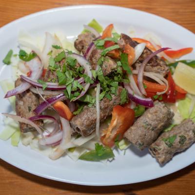 A plate of kebabs with onions, red peppers, and herbs.