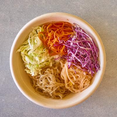 A bowl of noodles with shredded cabbage and grated carrots.