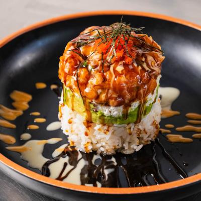 Layered sushi tower with crabmeat and avocado on a black plate drizzled with sauces.