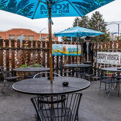 Outdoor bar patio featuring round mesh metal tables, chairs, and branded umbrellas.