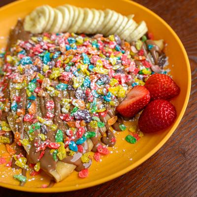 Fruity Pebble Crepe topped with chocolate and served with sliced banana and strawberries.