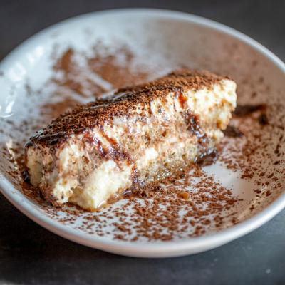 Slice of tiramisu dusted with cocoa powder on a white plate.