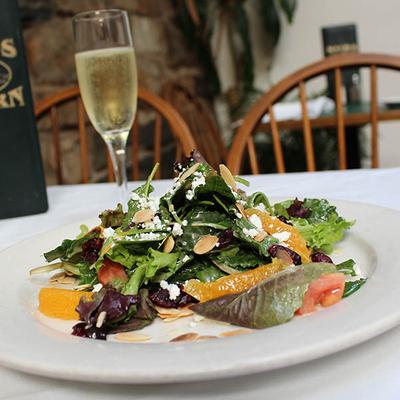 Mixed greens salad with orange slices, almonds, and cheese, accompanied by sparkling wine.