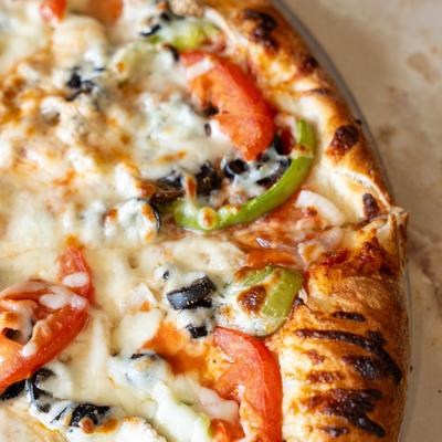 Vegetable pizza with melted cheese, bell peppers, tomatoes, and olives.