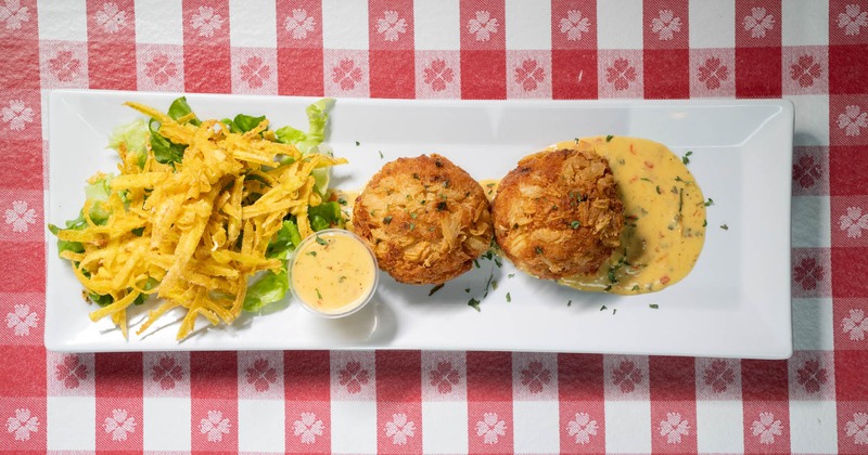 Crab cakes with salad and creamy dipping sauce on a white plate