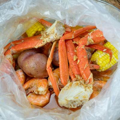 Clear plastic bag filled with crab legs, shrimp, red potatoes, and corn.