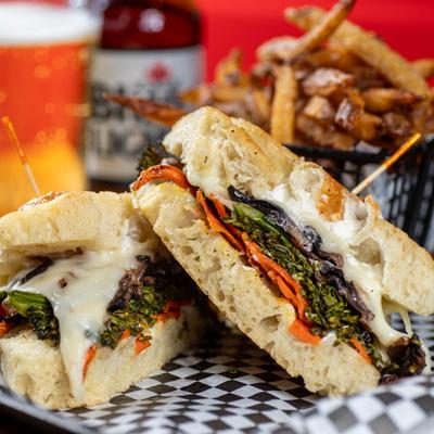 A close up of the veggie sandwich with fries and beer in background.