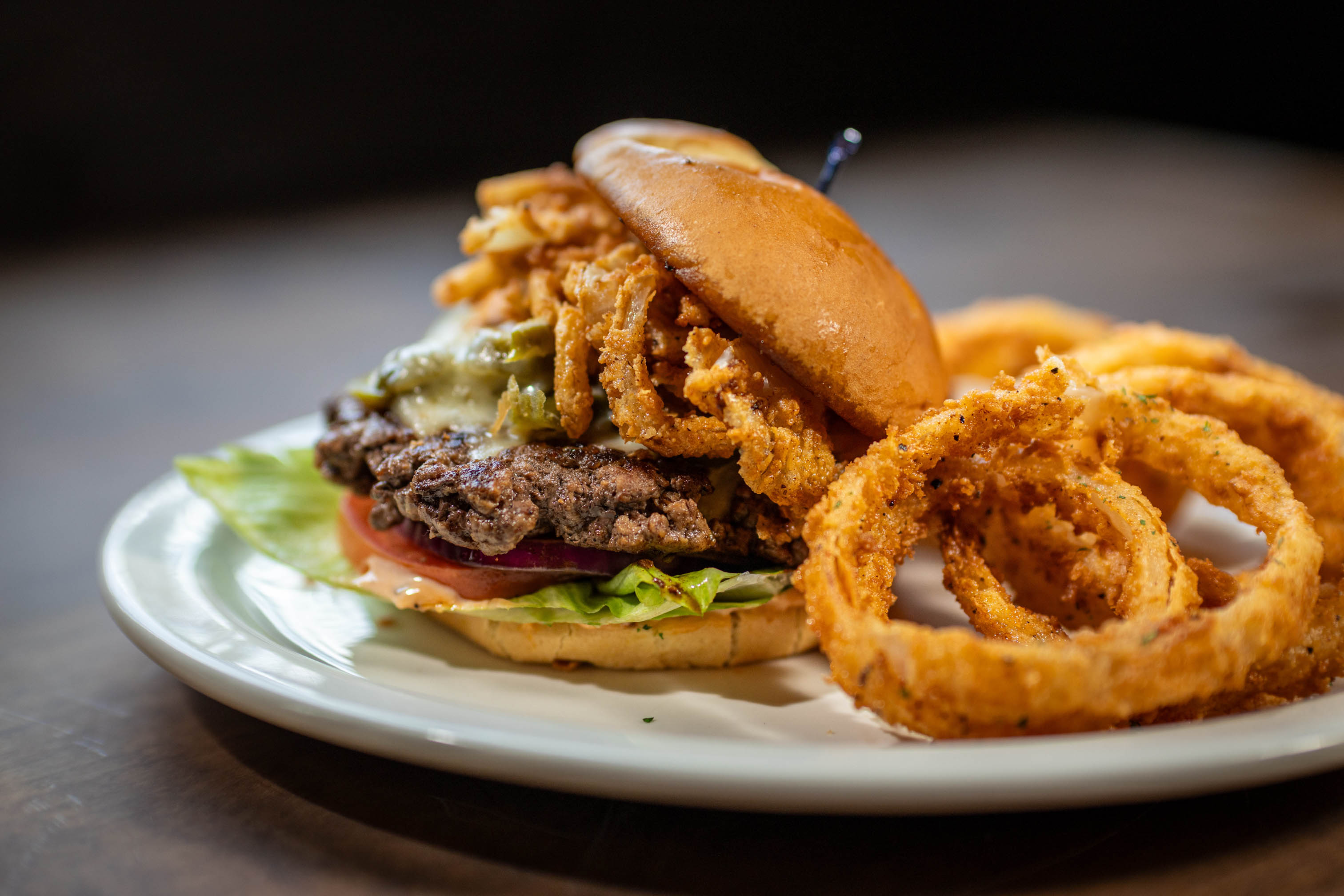 A gourmet burger topped with crispy onion straws served alongside golden onion rings