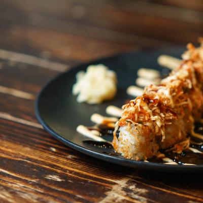 Sushi roll drizzled with sauce on a black plate.