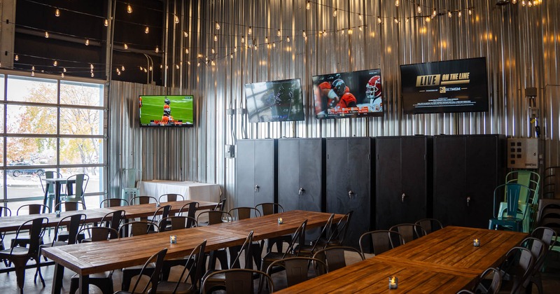 Interior, long table setups with chairs, metal coated wall, TVs on the wall