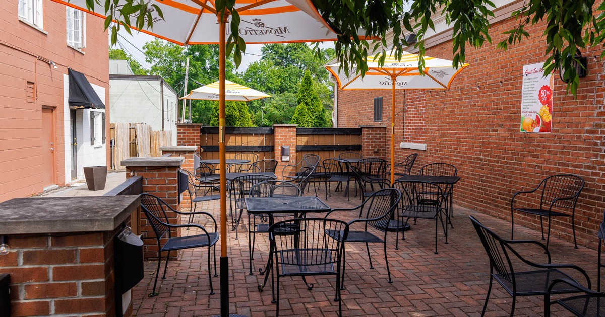 Outdoor brick patio with tables, chairs, umbrellas, and red brick walls.