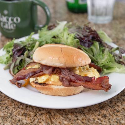 Breakfast sandwich with scrambled eggs, bacon, and a side of greens.