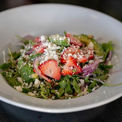 Salad with arugula, strawberries, avocado, red onion, goat cheese, and walnuts.