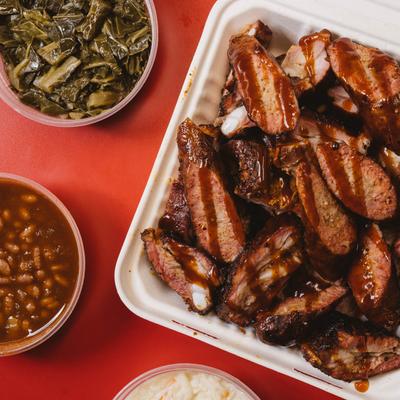 A platter of ribs and sausage with sides of collard greens and baked beans.