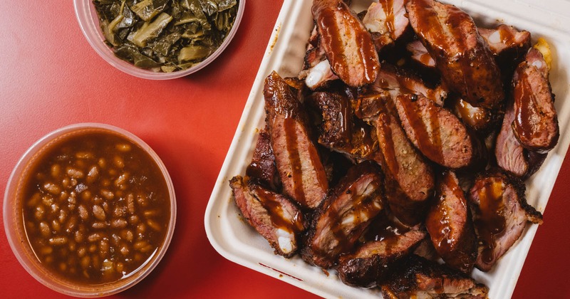 Pork hot link ribs on top of a bed of fries, with baked beans and collard greens