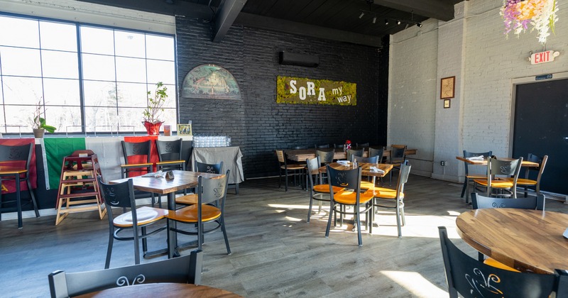 Interior, dining area with brick walls, big windowpanes, wooden chairs and tables and decorations