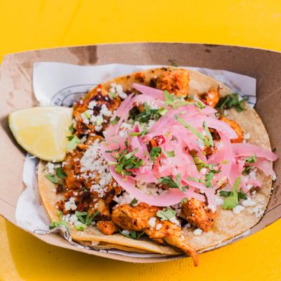 Chicken taco  served on a tortilla in a paper boat.