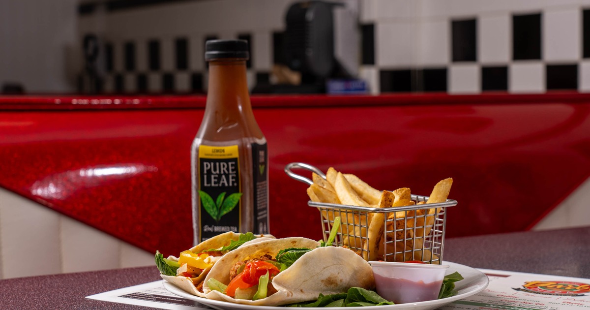 Two filled tacos, French fries in a basket, and iced tea on a plate