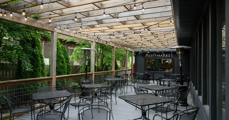 Outdoor patio area with tables and chairs under a pergola, with string lights