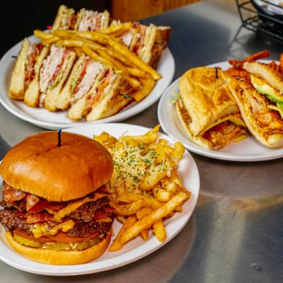 Assorted deli sandwiches served with fries on metal table.