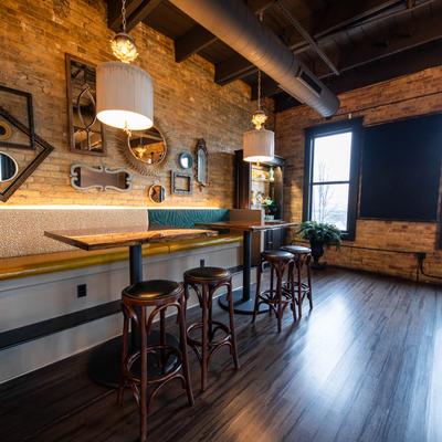 Interior, banquette, tables and bar stools by a brick wall decorated with mirrors and frames.
