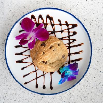 Chocolate chip cookie garnished with two flowers.