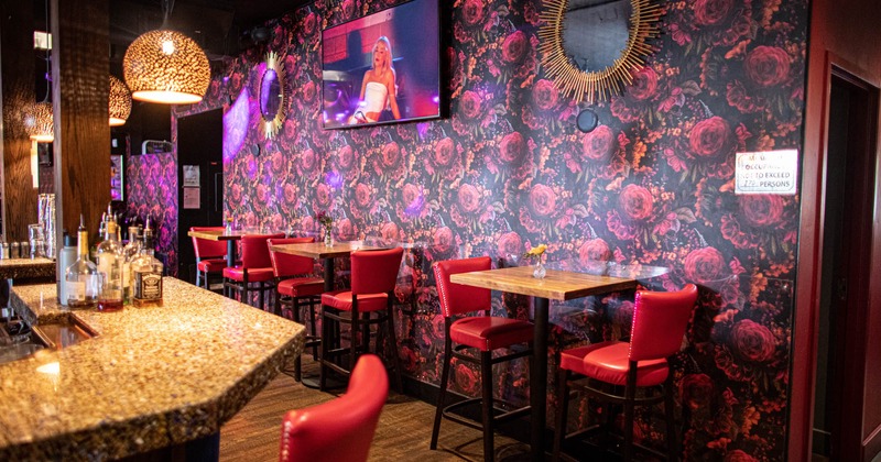 Interior, bar area, high wooden top tables with stools, colorful wallpaper, TV on the wall