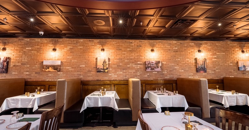 Interior of a restaurant with booths, white tablecloths, and a brick wall featuring framed photos