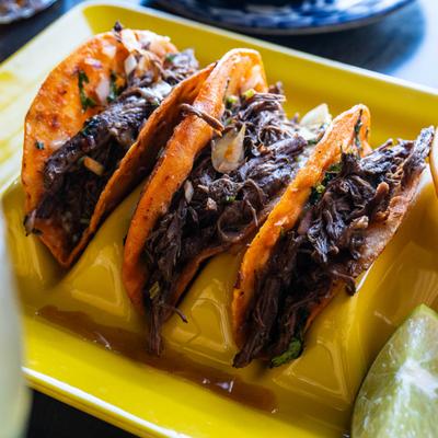 Three cheese and birria tacos on a yellow holder.