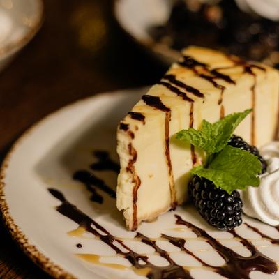 A slice of cheesecake with whipped cream, mint, and a blackberry.