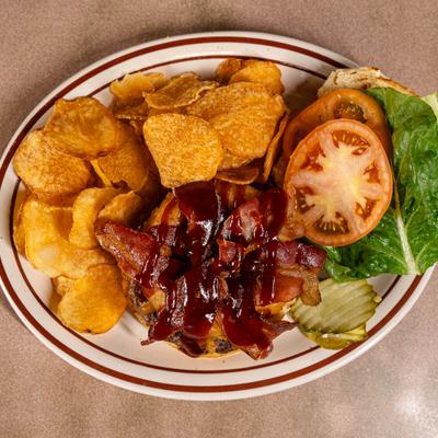Top view of a bacon cheeseburger with chips, lettuce, tomatoes, and pickles.