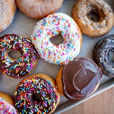 A tray of assorted donuts with colorful sprinkles, chocolate, and glazed toppings on a wooden table.