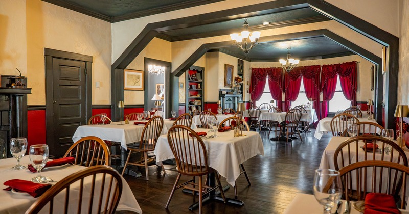 Elegant dining room with tables, red drapes, chandeliers and classic wooden chairs