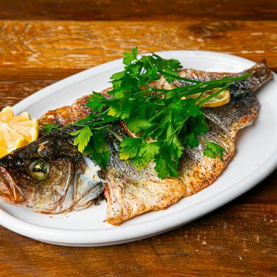 A grilled branzino garnished with parsley and lemon on a plate.