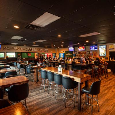 Bar interior with wooden tables, black chairs, and TVs.