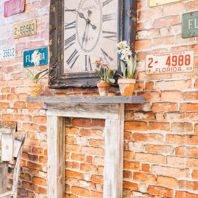 Rustic brick wall decorated with a vintage-style rectangular clock and wood mantel shelf.