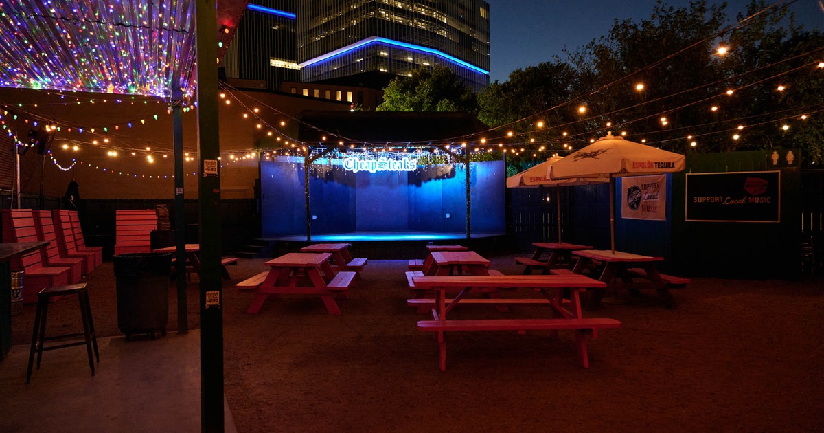 Exterior, outdoor stage, wooden tables with benches, lantern decoration, neon restaurant logo