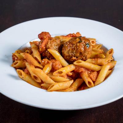 Penne pasta topped with tomato sauce and two meatballs.