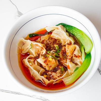 Pork long bao in chili oil, garnished with bok choy.