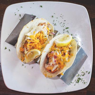 Two tacos with shredded cabbage, orange cheddar cheese and lemon slices.