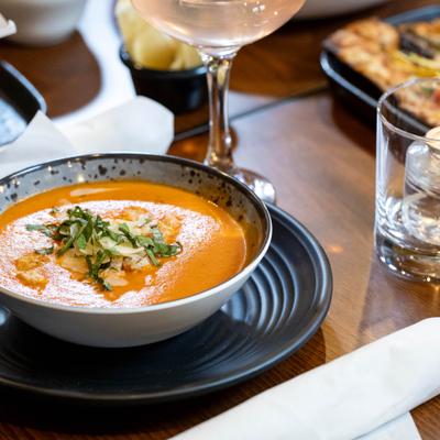 Tomato bisque topped with Parmesan and basil, served with a cocktail.