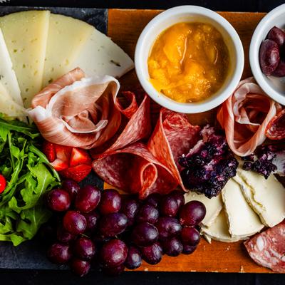 Assorted meats, cheeses, grapes, olives, and spreads arranged beautifully on a wooden board.